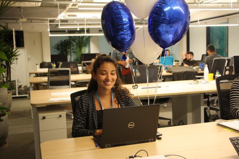 Fernanda sentada em uma mesa olhando para seu notebook e sorrindo